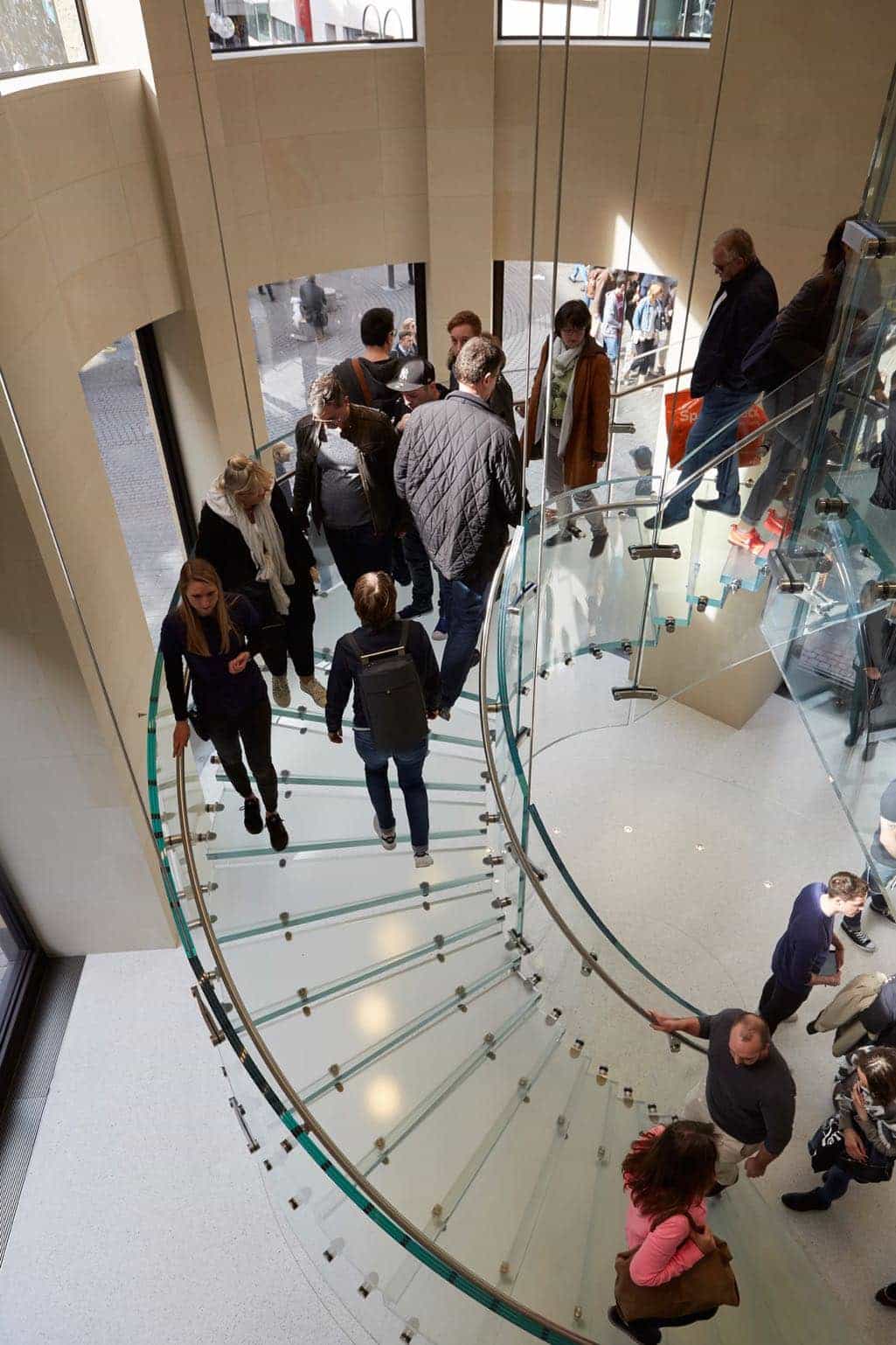 The double height grand hall of Apple Schildergasse in Cologne features a circular, suspended glass stair case.