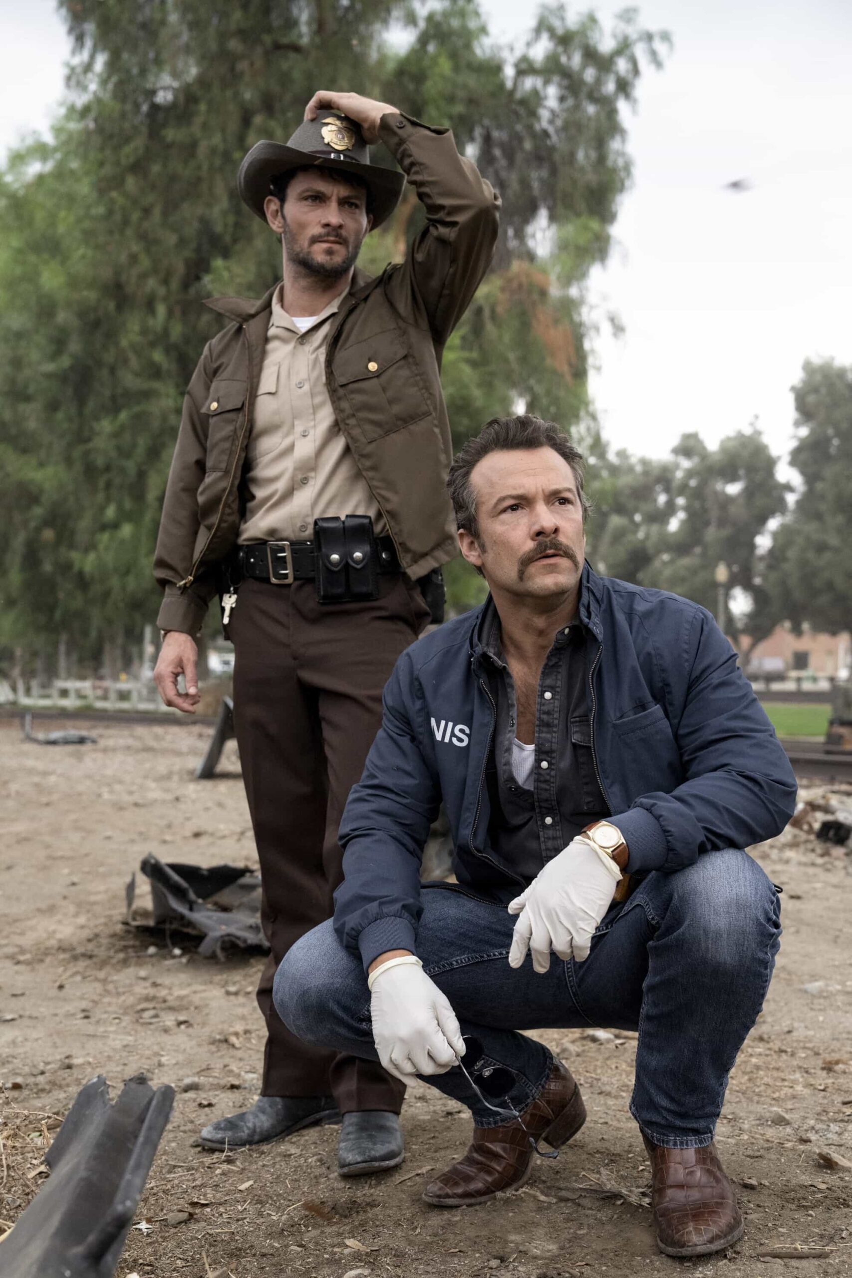 NCIS Origins Season 2 Episode 5 “Funny How Time Slips Away” – When a naval officer mysteriously dies in the ‘90s, Gibbs (Austin Stowell) and the team travel to the small dust-blown town of Serenity, Calif., where they encounter secret-harboring residents, an uncooperative sheriff and an investigation that will reverberate for decades, on the first part of the NCIS crossover event on NCIS: ORIGINS, Tuesday, Nov. 11 (8:00-9:00 PM, ET/PT) on the CBS Television Network, and streaming on Paramount+ (live and on demand for Paramount+ Premium plan subscribers, or on demand for Paramount+ Essential subscribers the day after the episode airs)*. Mark Harmon returns to the role of Gibbs in a special guest appearance.  Pictured (L-R): xxx and Kyle Schmid as Mike Franks.  Photo: Greg Gayne/CBS ©2025 CBS Broadcasting, Inc. All Rights Reserved.