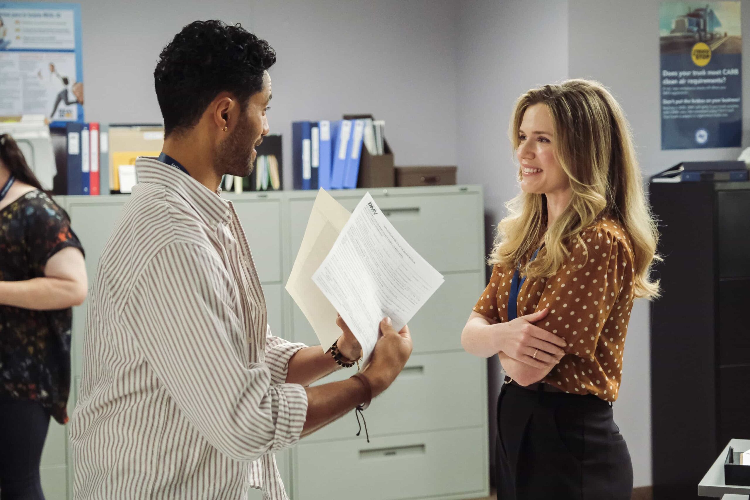 DMV Season 1 Episode 7  “There Is No I in DMV” – Barb takes the team on a field trip to the rival North Hollywood branch to learn the secrets of their success. She begins to doubt herself after meeting their charismatic manager, Beau (Randall Park). Meanwhile, Gregg and Vic get in Colette’s head that Noa prefers risk-takers, on DMV, Monday, Nov. 24 (9:30-10:00 PM, ET/PT) on the CBS Television Network, and streaming on Paramount+ (live and on-demand for Paramount+ Premium plan subscribers, or on-demand for Paramount+ Essential subscribers the day after the episode airs)*. Pictured L to R: Alex Tarrant as Noa and Harriet Dyer as Colette. Photo: Bertrand Calmeau/CBS ©2025 CBS Broadcasting, Inc. All Rights Reserved.