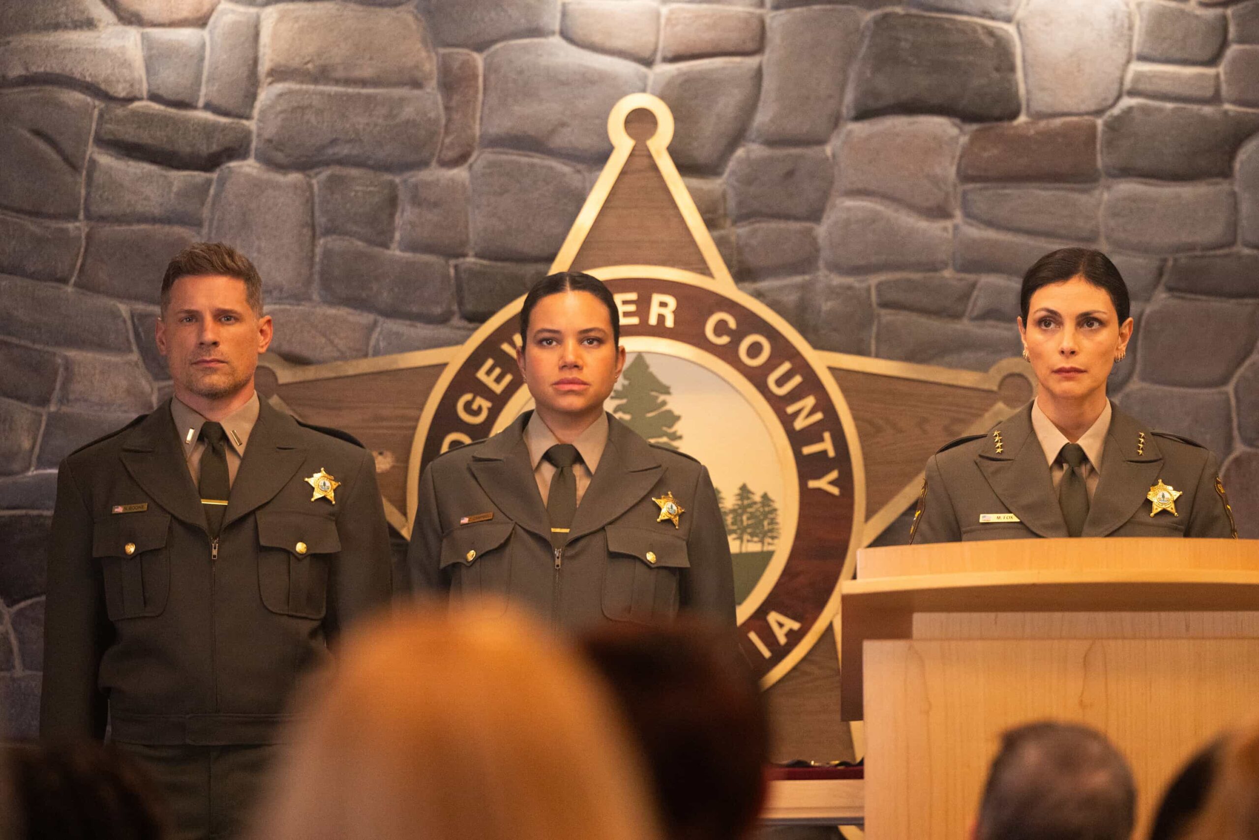 Sheriff Country Season 1 Episode 11 “The Aftermath” – When a courthouse security test ends in a shocking murder, Sheriff Mickey Fox uncovers a dangerous conspiracy reaching deep into Edgewater’s justice system.Pictured: Matt Lauria as Boone, Michele Weaver as Cassidy Campbell and Morena Baccarin as Sheriff Mickey Fox. Photo: Darren Goldstein/CBS ©2025 CBS Broadcasting, Inc. All Rights Reserved.