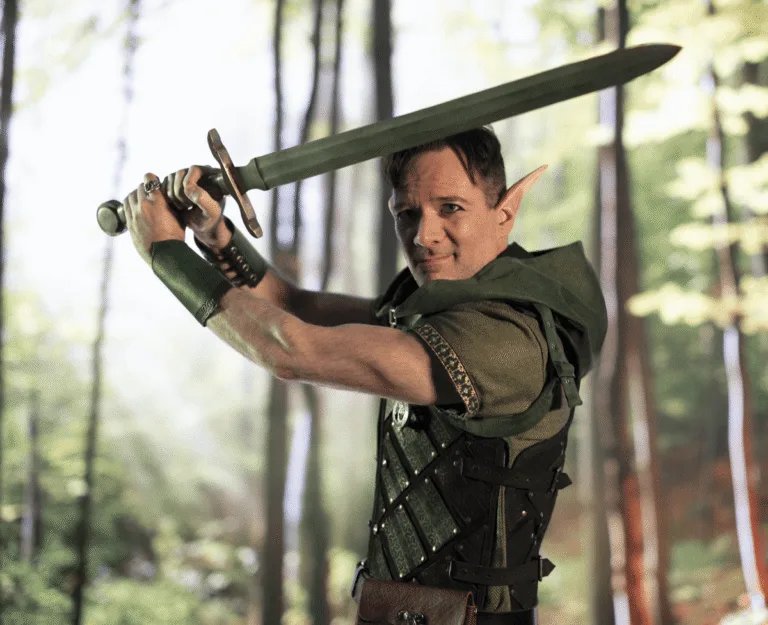 Alt: Man in elven warrior costume raising sword in forest