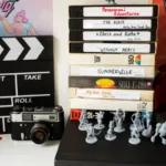 Stack of vintage VHS tapes next to clapperboard and miniatures